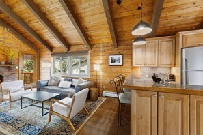 A cozy cabin interior with a wooden ceiling, a fireplace, a sofa, a dining area, and a kitchen with wooden cabinets and a refrigerator. - Cozy Duplex in West Vail – Near Vail Village (Vail)
