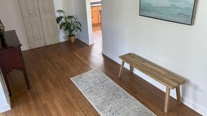 En hall med trägolv, en bänk, en matta, en dörr och en krukväxt.