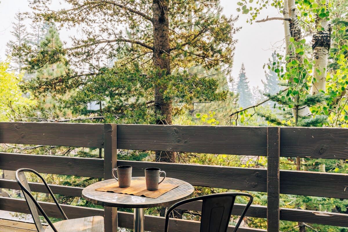 A wooden deck with a round table and two chairs, overlooking a forested area.