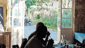 A dining area with a table set for two, a stone wall, and a view of a garden through a large open door. - Le Mas d'Ayen (Ayen)