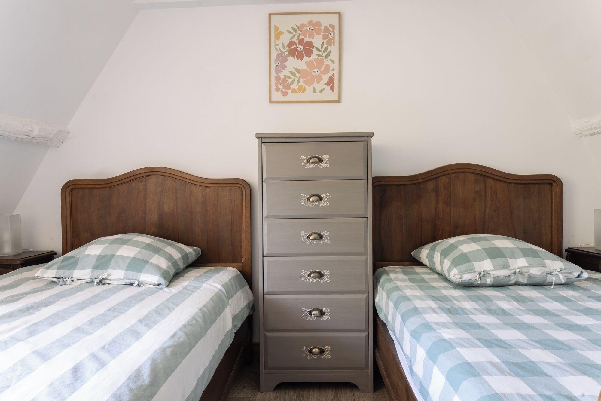 A bedroom with two beds, a dresser, and a floral artwork on the wall.