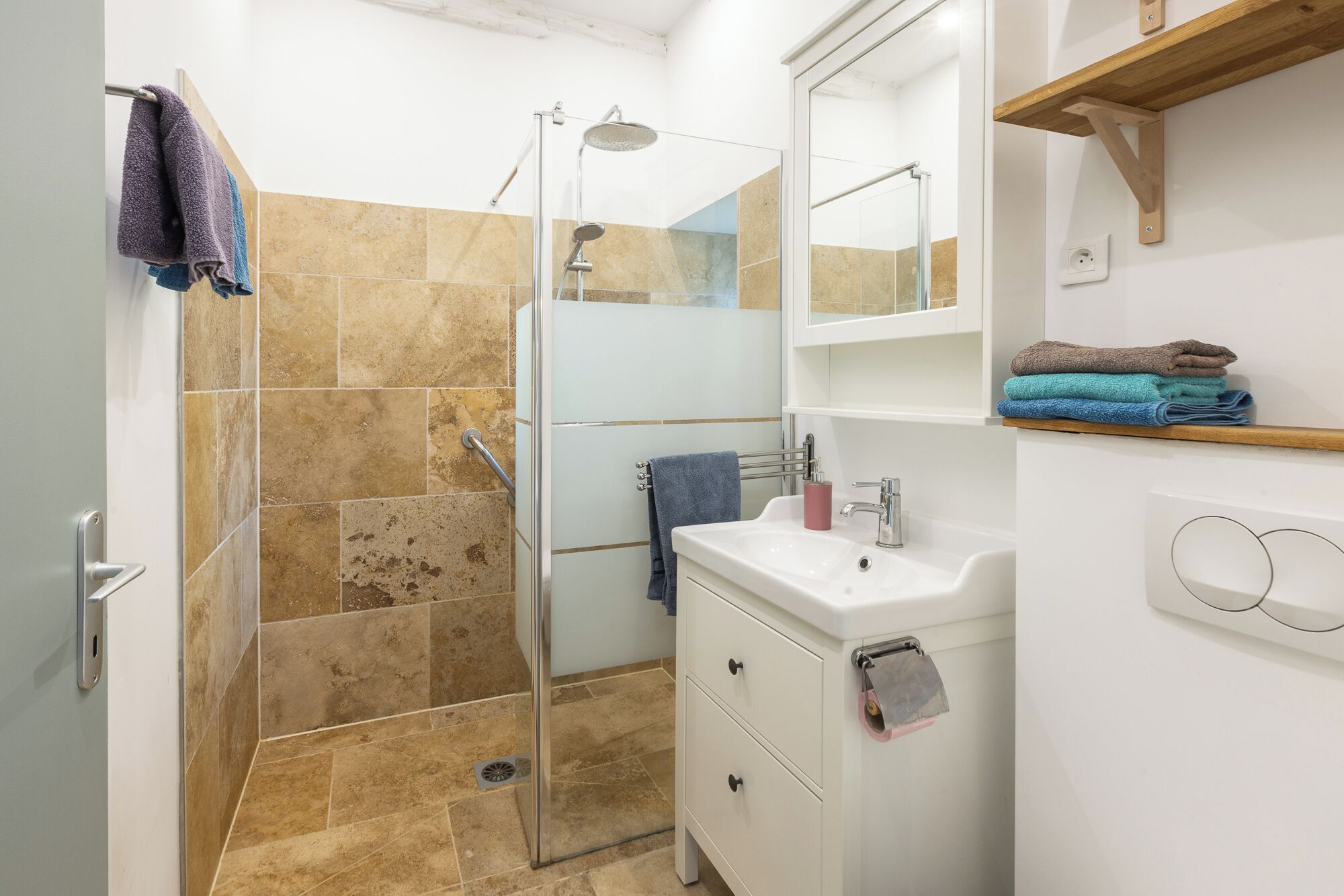 A bathroom with a glass shower enclosure, a sink, a mirror, and a towel rack.