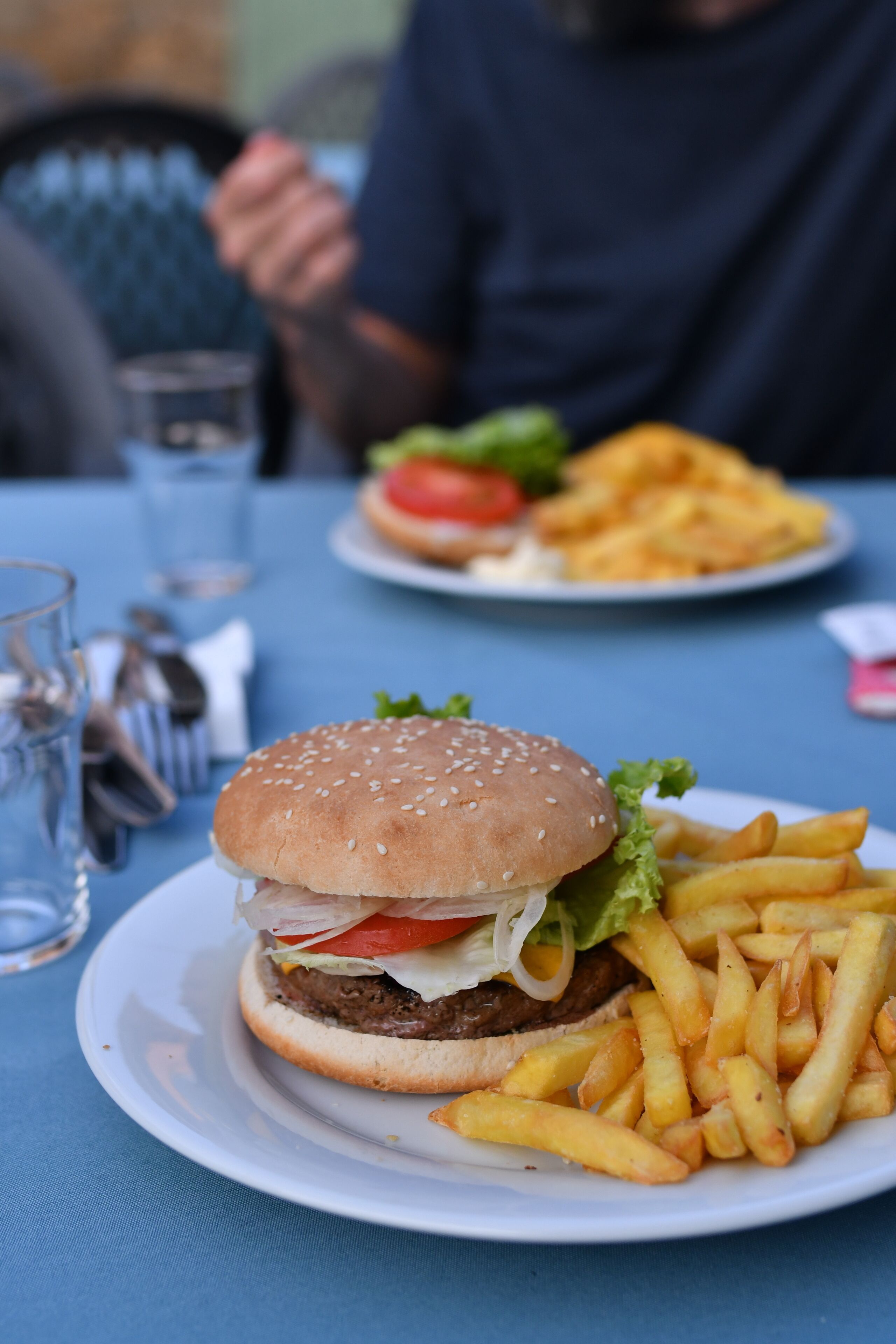 Un repas composé d’un hamburger et de frites servis dans une assiette, un verre d’eau et une fourchette posés sur une table.