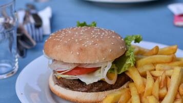 Un repas composé d’un hamburger et de frites servis dans une assiette, un verre d’eau et une fourchette posés sur une table.