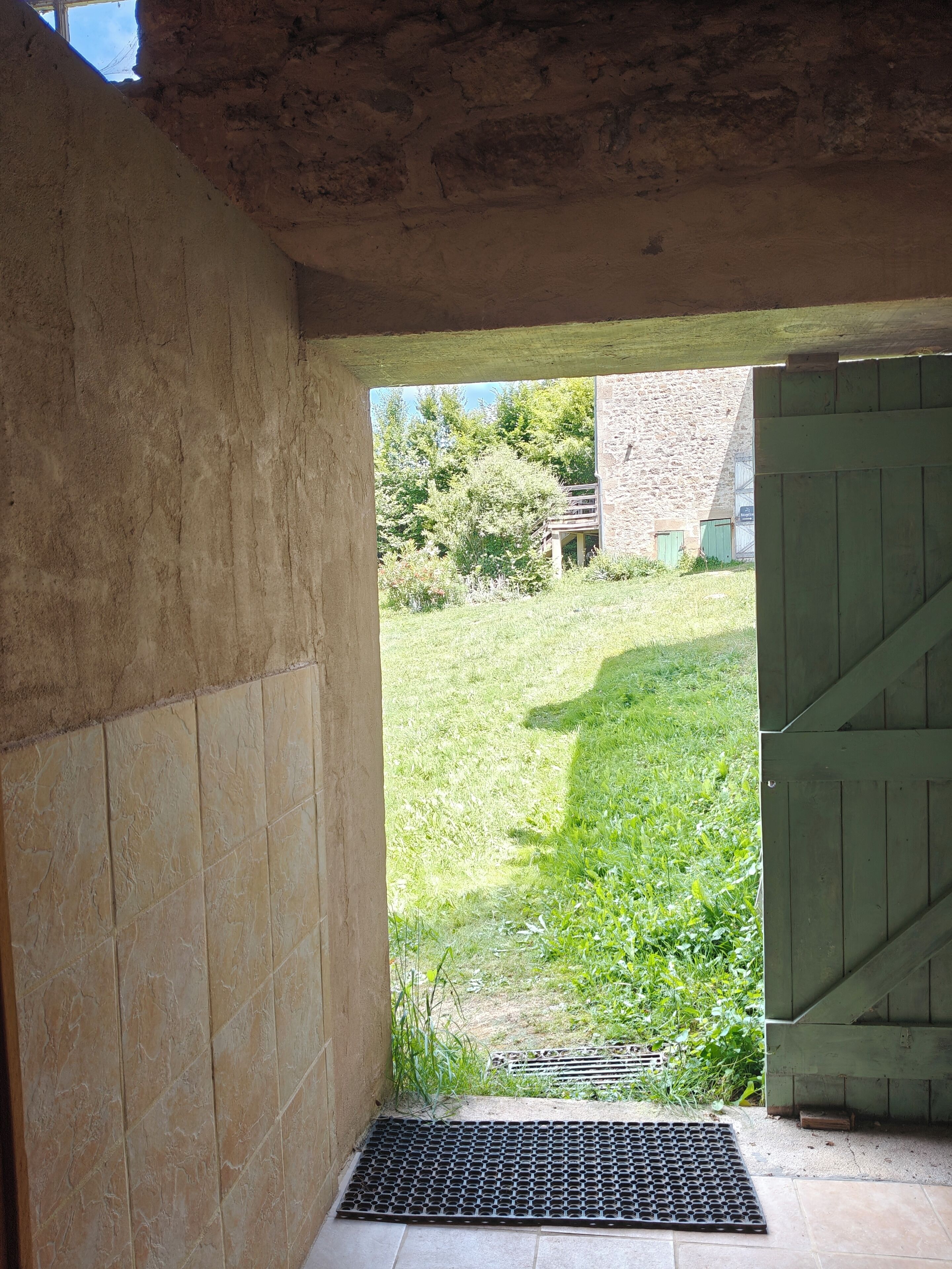A doorway leading to a grassy area with a stone wall and a green gate.