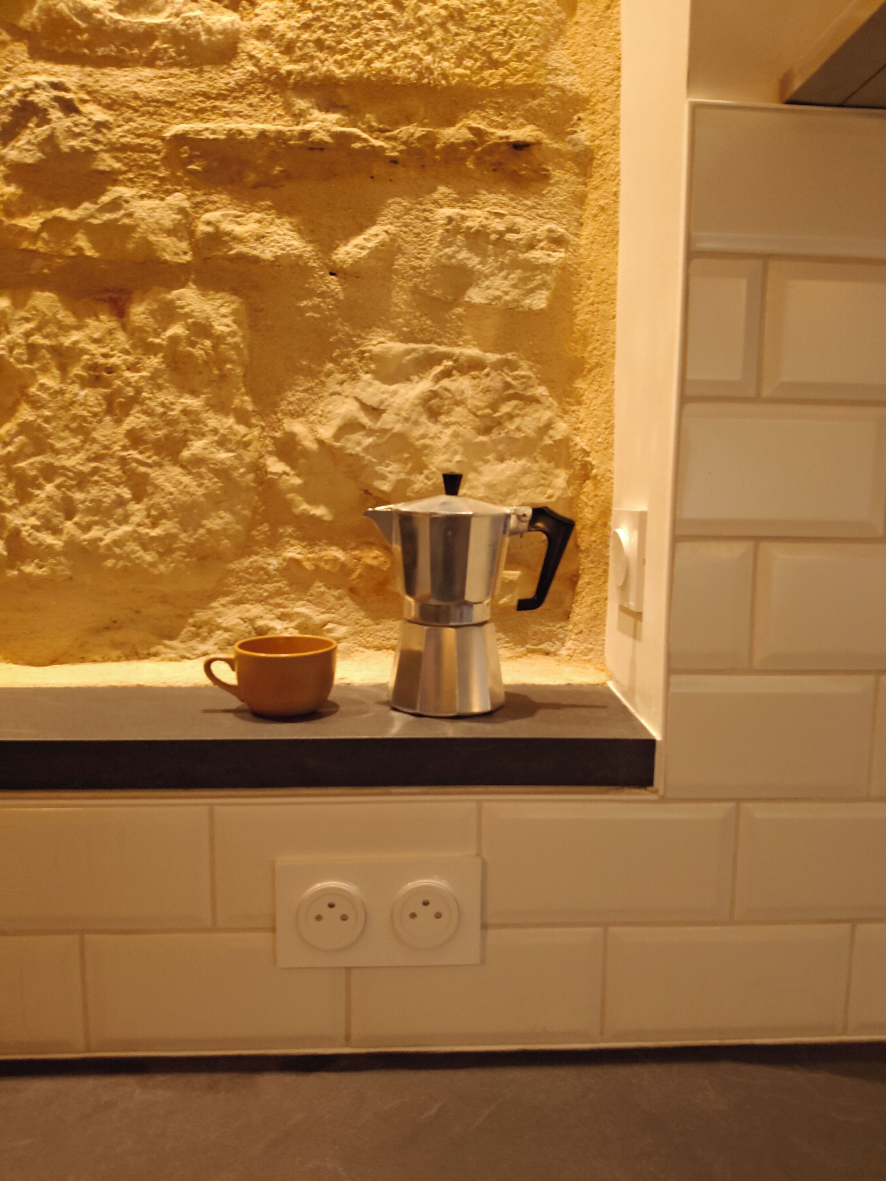 A kitchen with a coffee maker and a cup on the counter, a textured wall, and a white tiled backsplash.