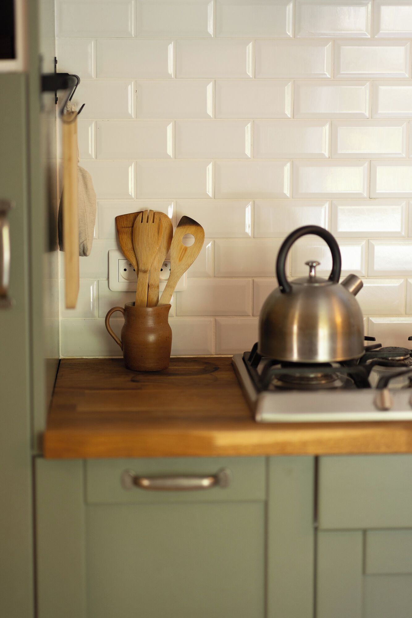 A kitchen with a wooden countertop, a kettle, a pot, and wooden utensils.