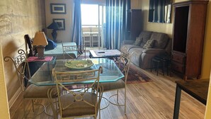 A living room with a glass dining table, chairs, a sofa, a TV, and a wooden cabinet.