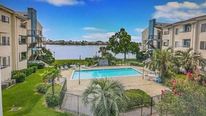 A residential building with a swimming pool, surrounded by greenery and a view of a body of water.