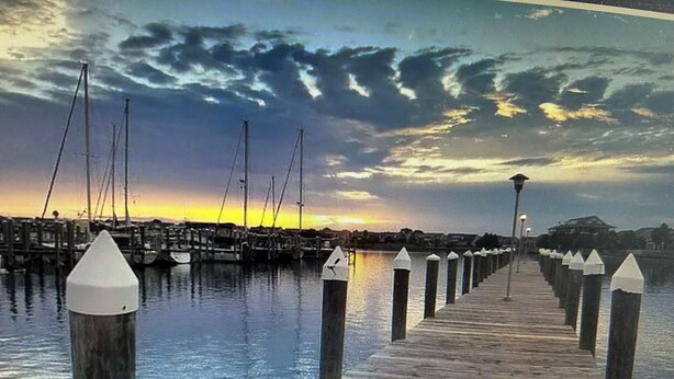 A wooden pier extending into calm water with boats docked at the end.