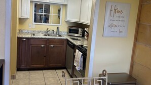 A kitchen with white cabinets, a microwave, and a toaster. There is a window above the sink, and a sign on the wall.