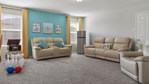 Een woonkamer met twee beige banken, een televisie, een lamp en een bowlingbaan.