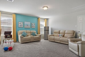 Ein Wohnzimmer mit zwei beigefarbenen Sofas, einem Fernseher, einer Lampe und einer Bowlinganlage.