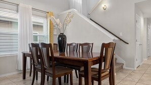 Een eetgedeelte met een houten tafel en stoelen, een vaas met bloemen en een trap op de achtergrond.