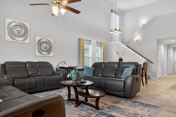 Ein geräumiges Wohnzimmer mit Deckenventilator, zwei Sofas, einem Couchtisch und einer Treppe, die zu einer weiteren Ebene führt.
