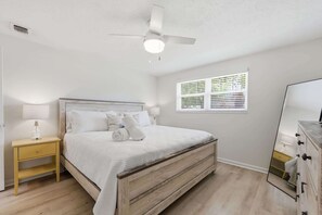 A bedroom with a bed, a nightstand, a ceiling fan, a window with blinds, and a dresser. - Liberty Breeze Retreat (Jacksonville Beach)