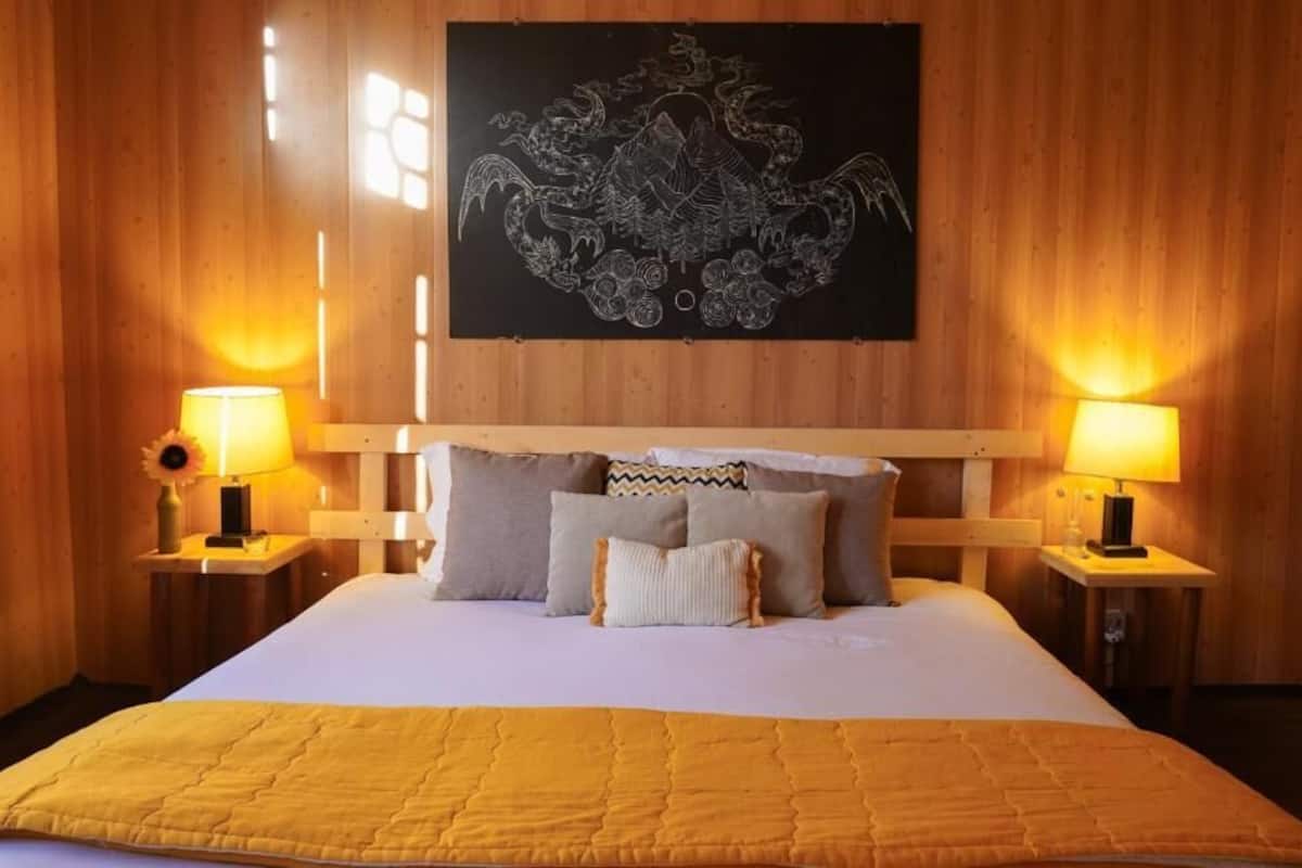 Una habitación de hotel con una cama grande, dos lámparas de noche, un cabecero de madera y una obra de arte colgada en la pared.