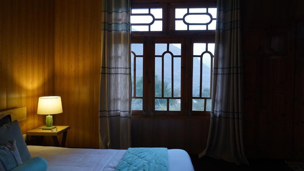 Une chambre avec un lit, une table de chevet avec une lampe et une fenêtre avec des rideaux.