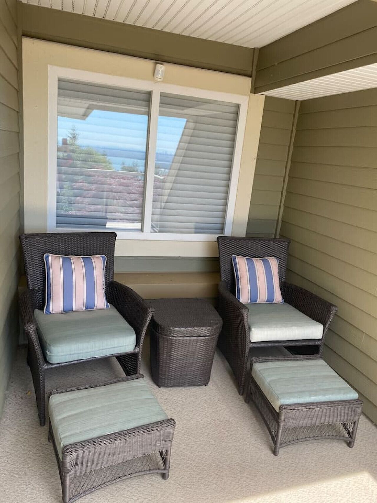 A covered outdoor seating area with wicker furniture and a window overlooking a residential area.