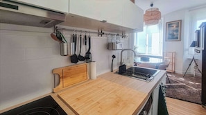 A modern kitchen with a wooden countertop, hanging utensils, and a view of the dining area.