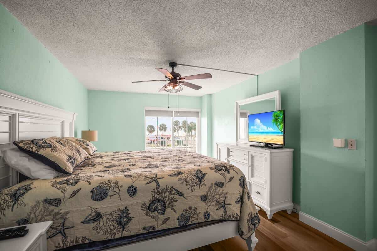 Un dormitorio con cama, ventilador de techo, televisor y vistas al exterior.