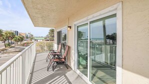 Un balcón con sillas, una puerta de cristal y vista a la playa y al paisaje urbano.