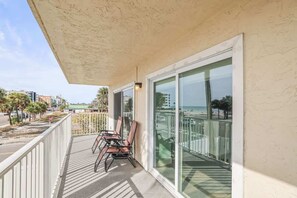Ein Balkon mit Stühlen, einer Glastür und Blick auf Strand und Stadtlandschaft.