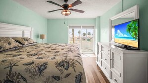 Un dormitorio con cama, ventilador de techo, televisión y vista al exterior.