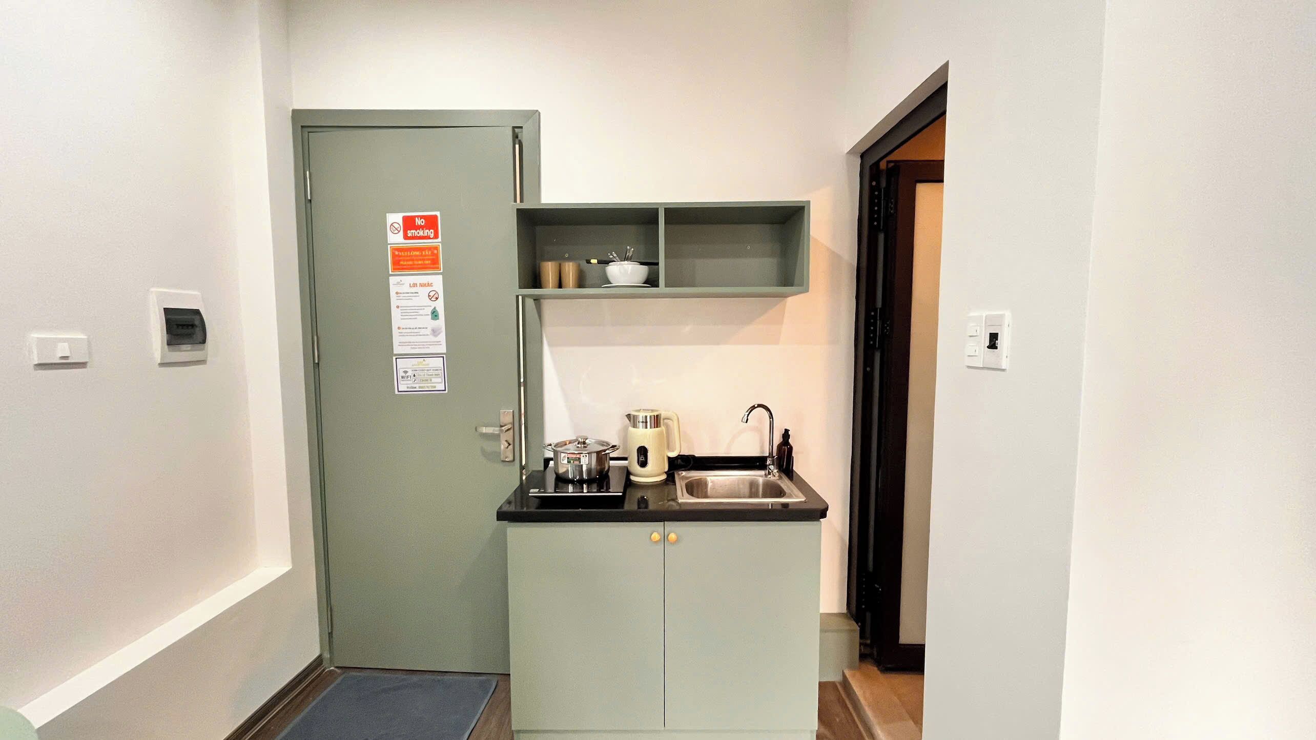 A compact kitchenette with a sink, a kettle, and a microwave. There is a door with a 'No Smoking' sign and a small shelf above it.