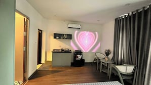 A hotel room with a kitchenette, a coffee machine, a small table with a chair, and a projection of a heart on the wall.