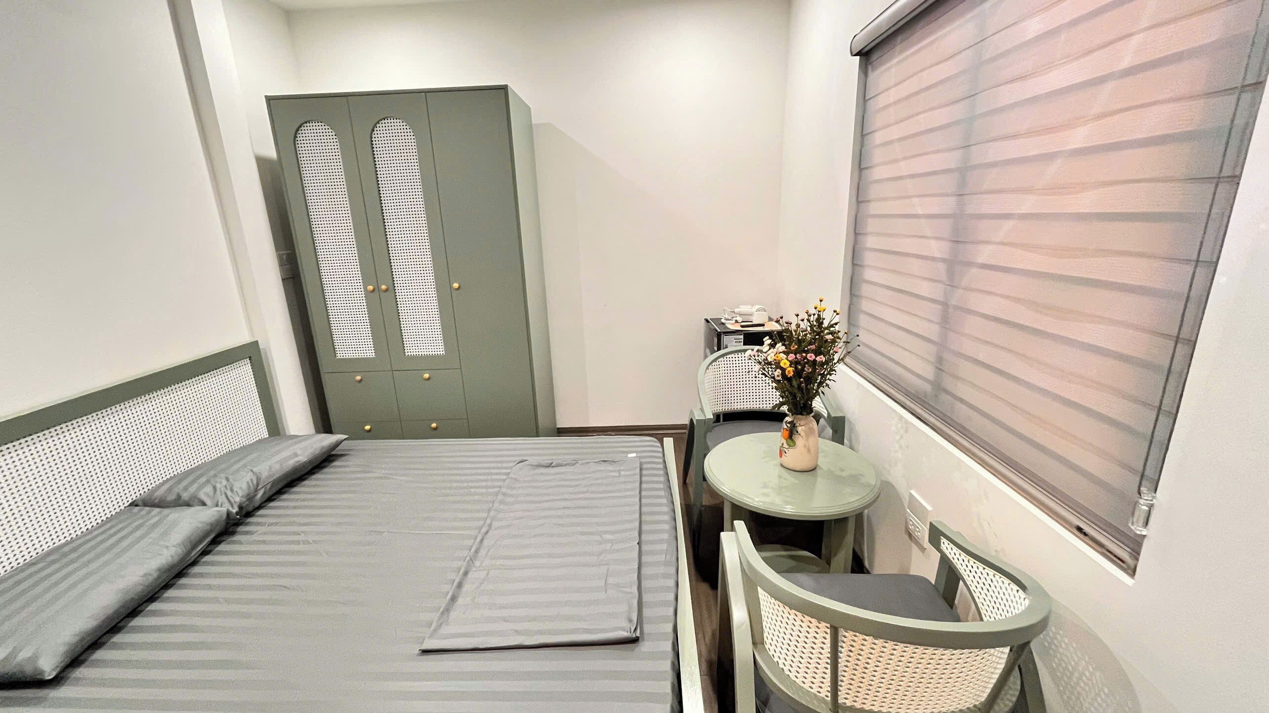 A compact room with a bed, a small table with a vase of flowers, a chair, and a wardrobe.
