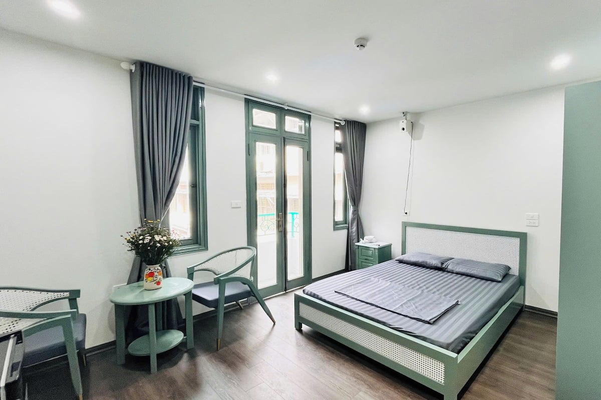 Un dormitorio con cama, una silla, una mesita y una ventana con cortinas.