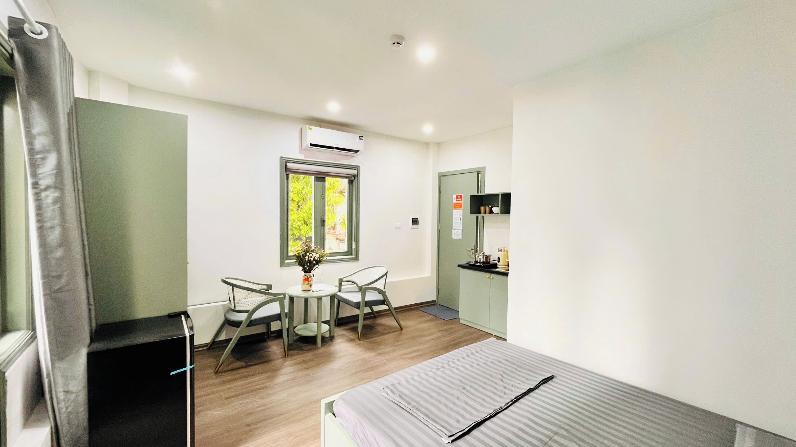 Una habitación pequeña con una cama, una mesa con sillas, un ventanal con vistas, un aire acondicionado y una kitchenette.