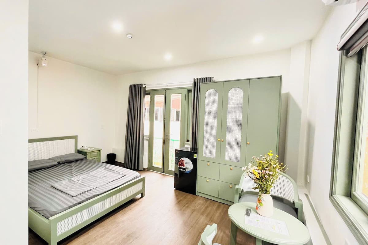 Un dormitorio con cama, una mesita de noche con un florero, un armario y una ventana.