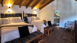 Ein Schlafzimmer mit zwei Betten, einer Bank, einem Sessel und einem durch eine Tür einsehbaren Badezimmer.