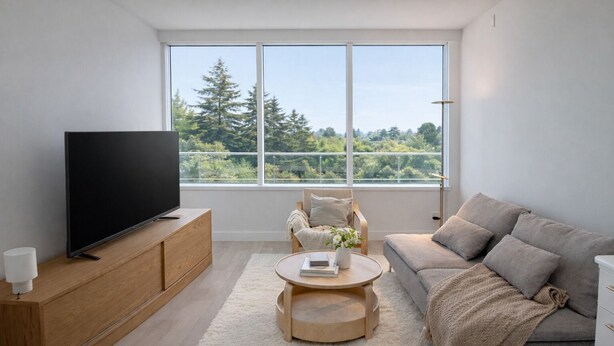 Ein modernes Wohnzimmer mit Flachbildfernseher, einer Holzkabine, einem runden Couchtisch, einem grauen Sofa und einem großen Fenster mit Blick auf Bäume.