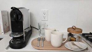 Eine Küchenarbeitsplatte mit einer Kaffeemaschine, zwei Tassen, einem Glas, einem Teller mit Besteck und einer Vorratsglas mit Deckeln.