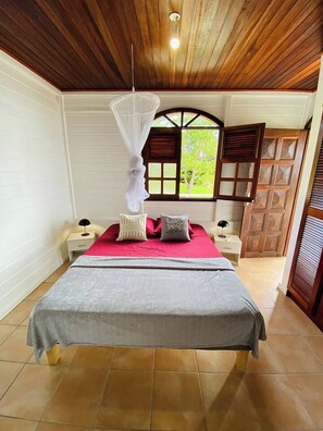 Un dormitorio con cama, ventana con vistas, techo de madera y mesita de noche con lámpara.