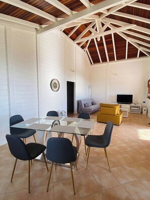 A spacious living area with a glass-top dining table, several chairs, a sofa, a TV, and a yellow cabinet. - 3-star villa - Perle des Hauteurs (Le Carbet)
