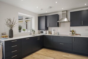 A modern kitchen with dark cabinets, a white countertop, a microwave, and a stainless steel range hood. - Premium Home, Garden & Parking, Nr Saunton Sands (Braunton)