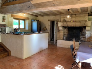Eine rustikale Küche mit Kamin aus Stein, Holzbalken, gefliestem Boden und einer Essecke mit Tisch und Stühlen.