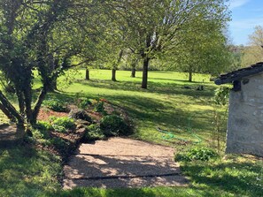 Ein Garten mit Kiesweg, Bäumen und einem Steinhaus.