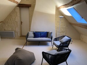 Ein Loft-Zimmer mit schrägen Wänden, einer Couch mit Kissen, einem Sessel, einer Stehlampe und einem Oberlicht.