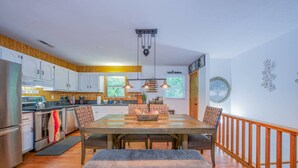 Uma cozinha moderna com armários de madeira, uma mesa de jantar com bancos, iluminação pendente e vista para o exterior.