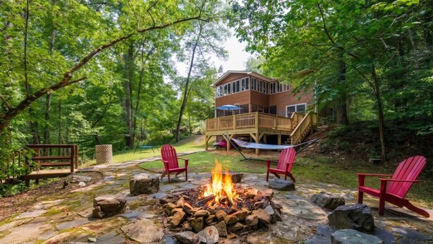 Uma cabana com lareira de pedra, cadeiras Adirondack vermelhas e um deck.