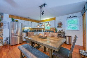 A modern kitchen with a wooden dining table, built-in appliances, and a 'Welcome' sign. - Riverfront Cabin, Fenced Yard, Firepit & Grill (Lake Lure)