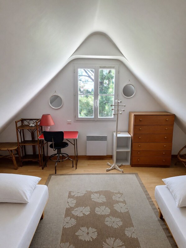 A dormitory room with a sloped ceiling, a desk, a chair, a dresser, and two beds.