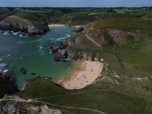 An aerial view of a coastal area with a beach, rocky cliffs, and a clear path leading to the beach.
