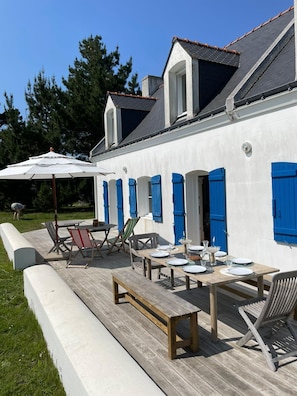 Ein weißes Gebäude mit blauen Fensterläden, einer Holzterrasse und Gartenmöbeln.