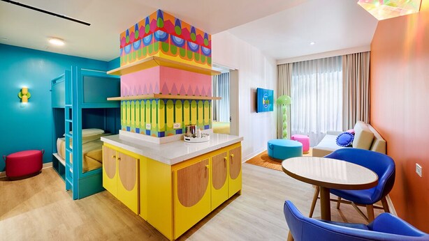 Una habitación luminosa y colorida con una cama litera, un armario amarillo, una mesa redonda y sillas azules.